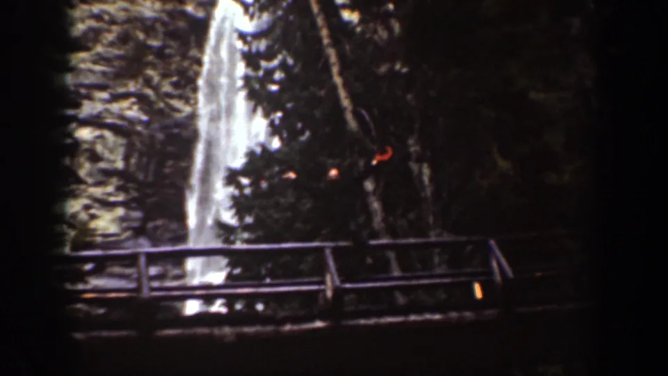 1939 Chelan, Washington home-movie frame showing a waterfall above a wooden bridge or railing in a shaded rocky gorge.