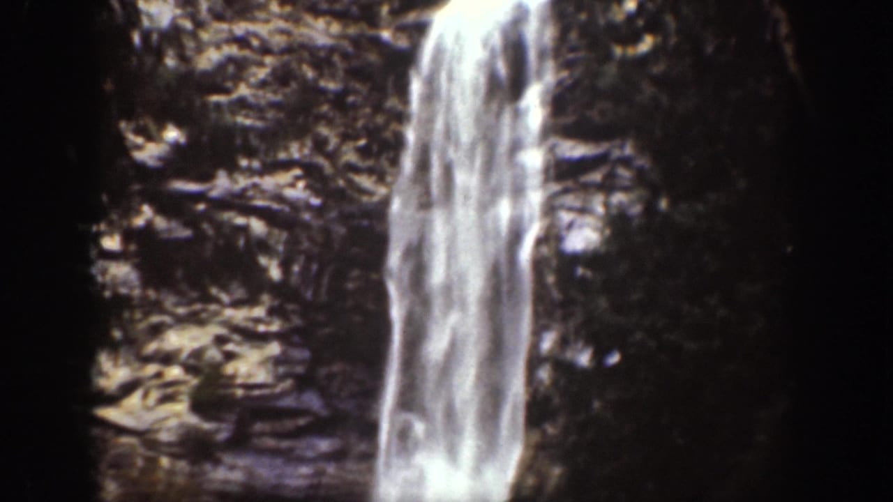 1939 Chelan, Washington frame showing a tall white waterfall descending along a layered rock face with trees at the edge.