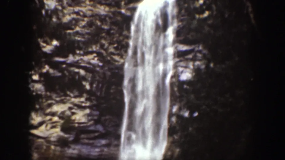 1939 Chelan, Washington frame showing a tall white waterfall descending along a layered rock face with trees at the edge.