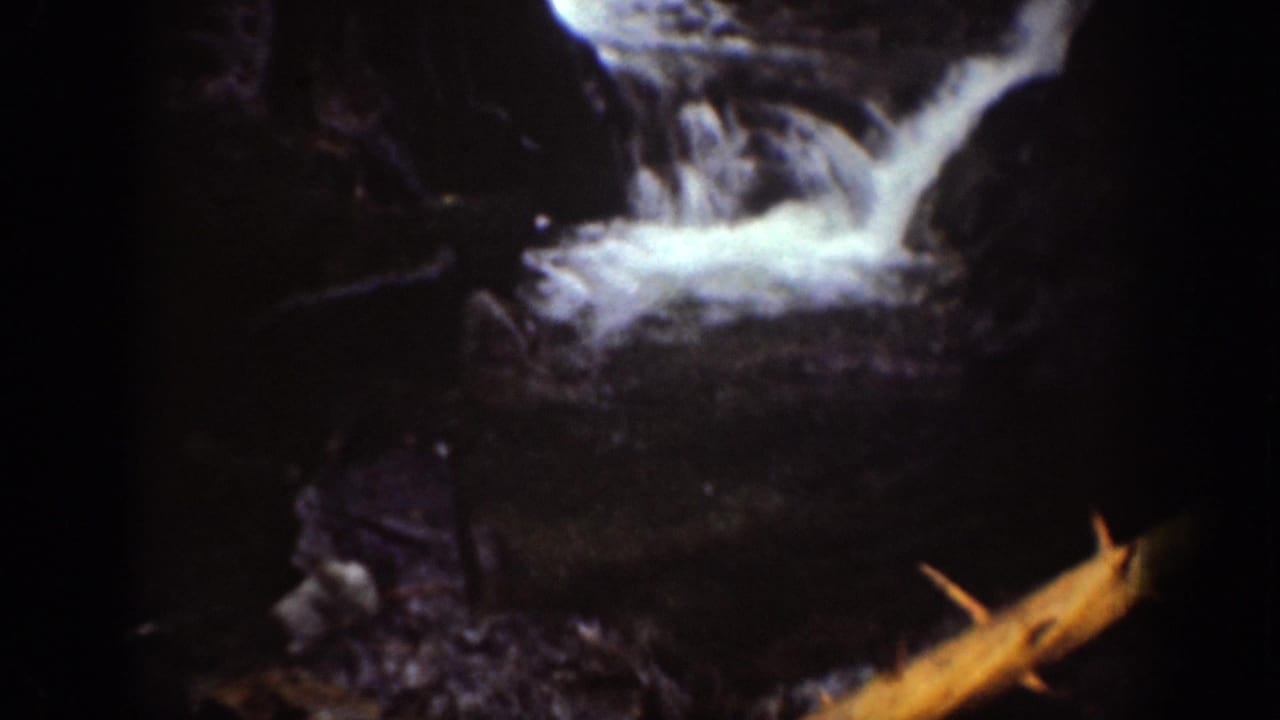 Chelan, Washington home-movie frame of a small cascade crossing dark rock with fallen debris visible.