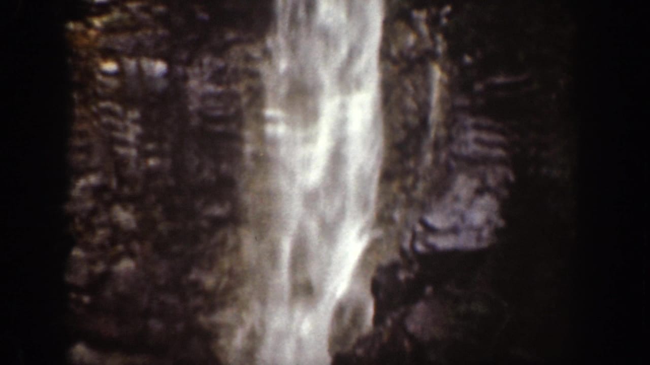 1939 Chelan, Washington 8mm frame showing a waterfall descending a shadowed rock face with bright sky or mist near the top.