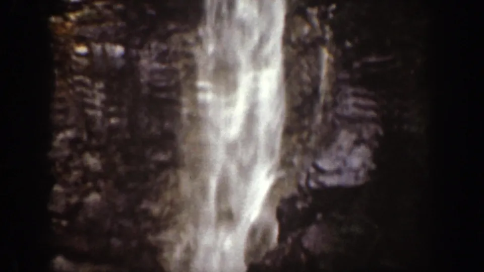 1939 Chelan, Washington 8mm frame showing a waterfall descending a shadowed rock face with bright sky or mist near the top.