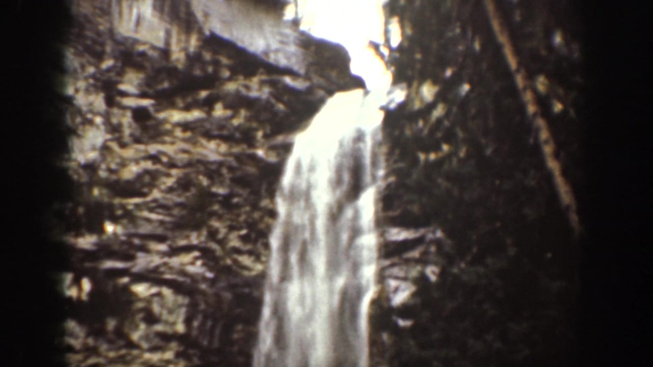 1939 Chelan, Washington 8mm frame with a vertical waterfall running down a textured rock wall beside dark forested edges.