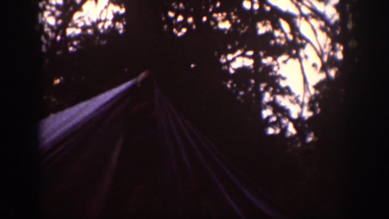 1939 Chelan home-movie frame showing a tent or tarp form under trees, partly silhouetted against patches of bright sky.
