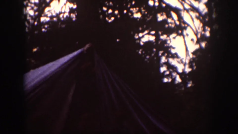 1939 Chelan home-movie frame showing a tent or tarp form under trees, partly silhouetted against patches of bright sky.