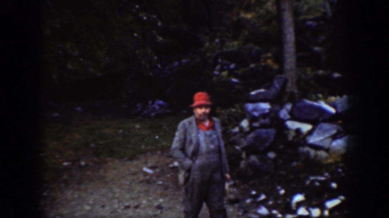 Adult male in red hat faces camera beside a dry-stone wall in a forested Pacific Northwest setting, circa 1939, Chelan, Washington.