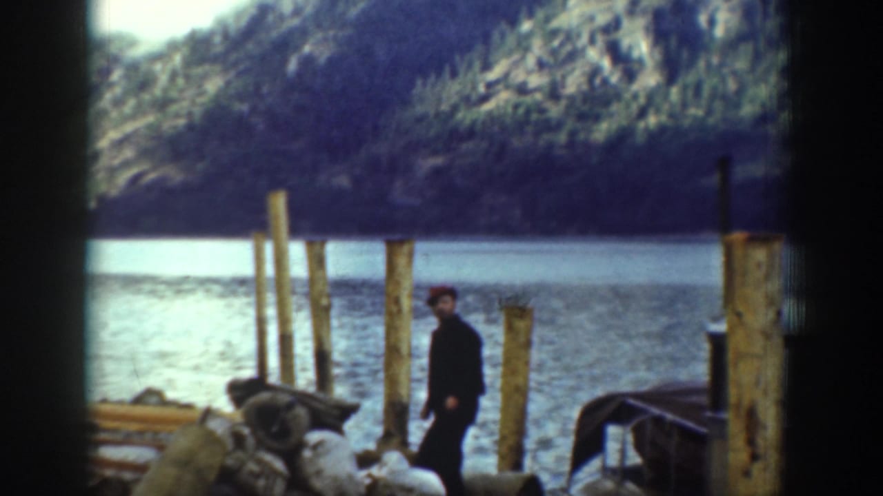 A lone man in dark clothing near wooden dock pilings beside a mountain lake; Chelan, Washington area, circa 1939 per metadata.
