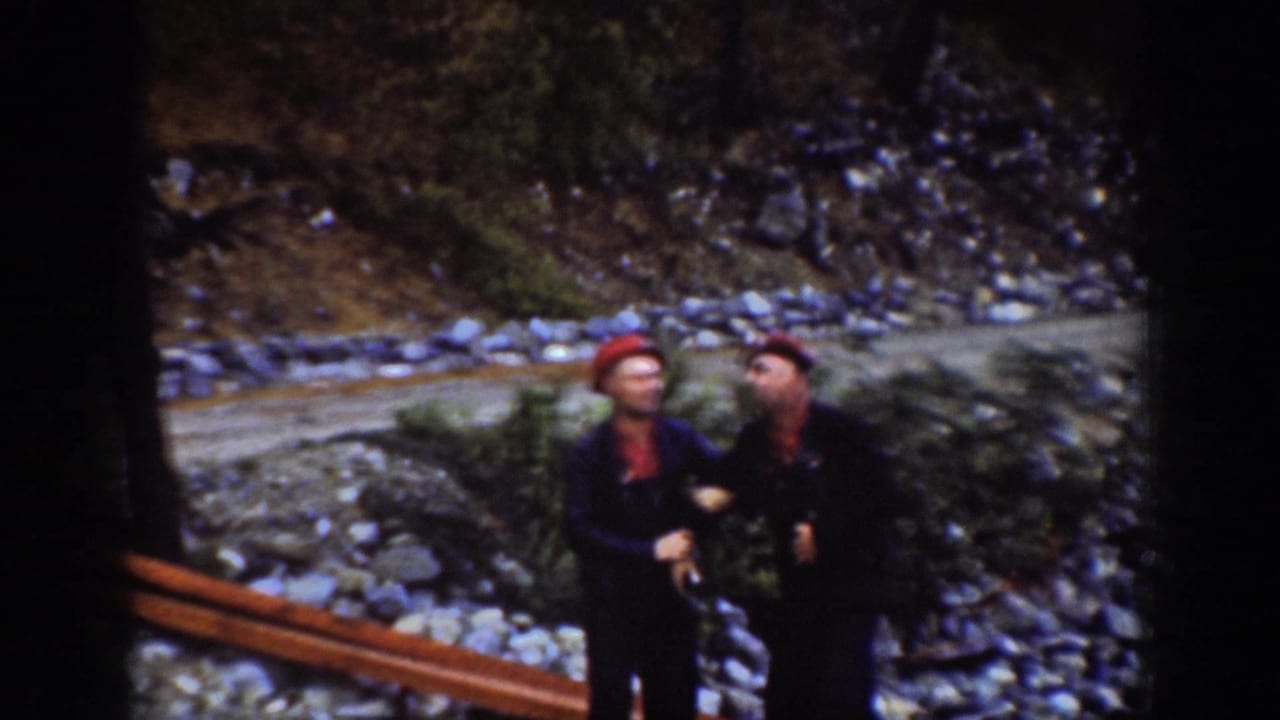 Two men in red knit caps and dark work coveralls face each other on a rocky shoreline near Chelan, Washington, circa 1939.