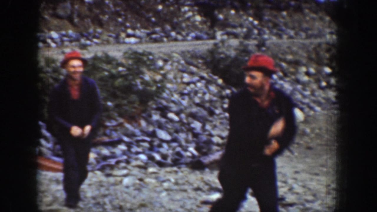 Two men in red work caps with arms raised in close physical exchange on a rocky shoreline near Chelan, Washington, circa 1939; both faces clearly visible.