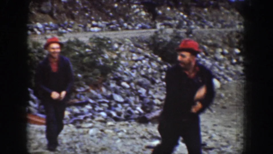Two men in red work caps with arms raised in close physical exchange on a rocky shoreline near Chelan, Washington, circa 1939; both faces clearly visible.