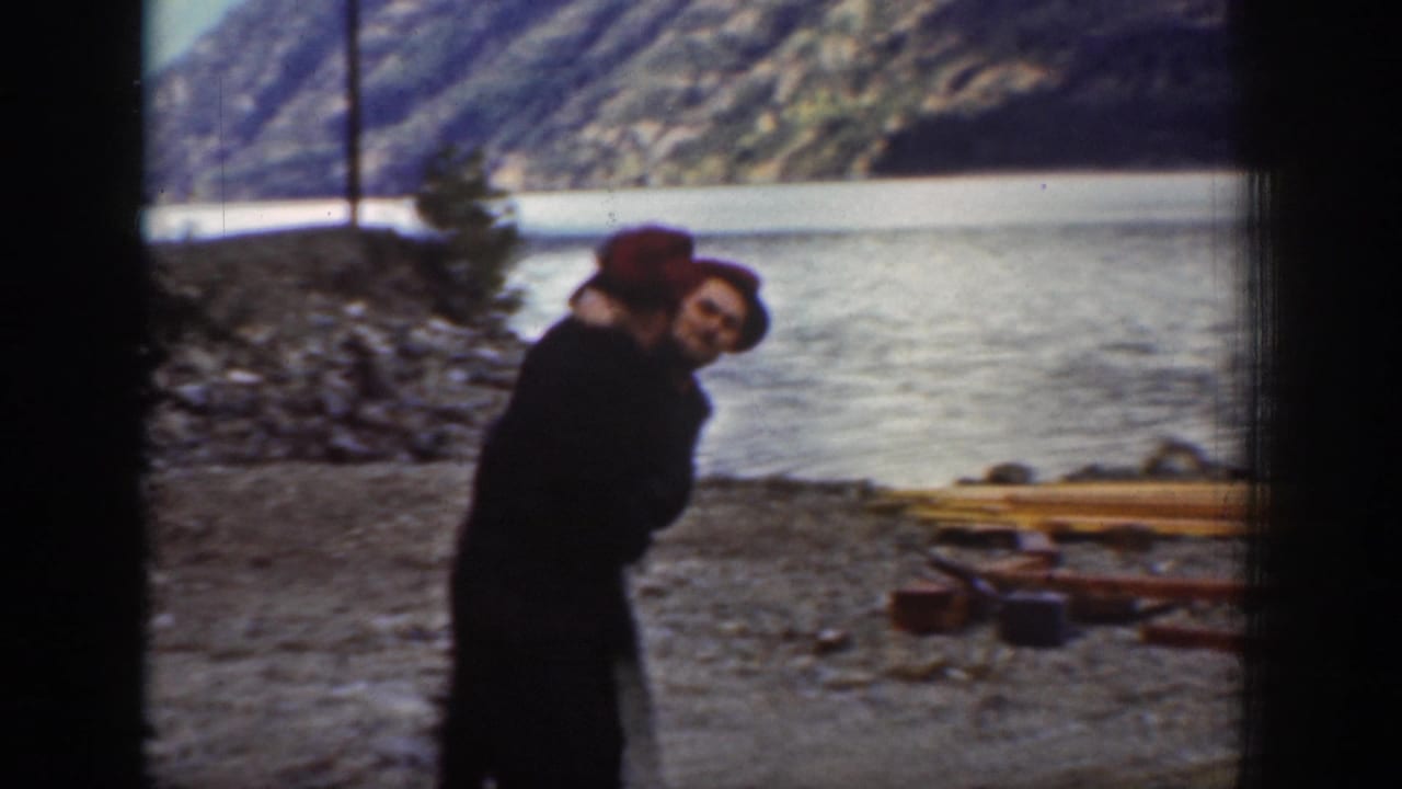 A tighter shot of one or two individuals, at least one wearing a red cap, on the rocky lakeshore near Chelan, Washington, circa 1939, with scattered timber and a mountain slope behind.
