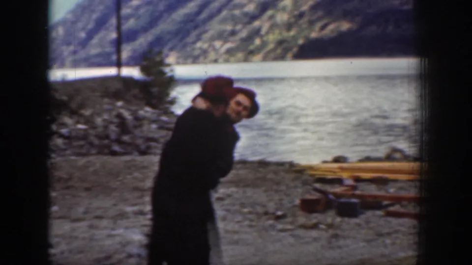 A tighter shot of one or two individuals, at least one wearing a red cap, on the rocky lakeshore near Chelan, Washington, circa 1939, with scattered timber and a mountain slope behind.
