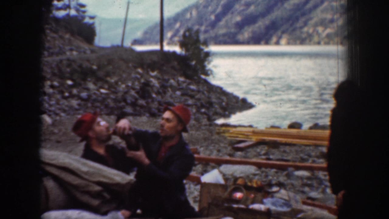 1939 8mm home movie: man in red bandana and dark clothing drinks from a bottle on a Washington lakeside, forested mountain slopes reflected in calm water behind.