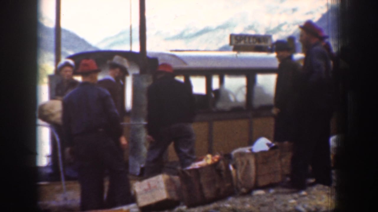 Workers load wooden crates alongside a touring bus at a mountain stop, Chelan, Washington, circa 1939; snow-capped peaks and a utility pole visible.