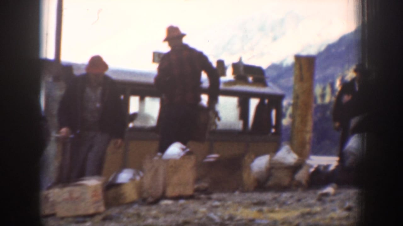 A worker in a pale hat oversees crates on a backlit platform, with a second figure in a red cap nearby and mountain peaks silhouetted, circa 1939 Washington.