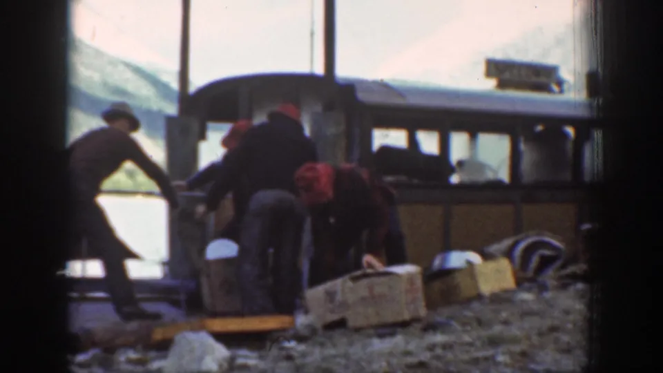 Workers stacking wooden crates alongside a bus or railcar at a mountain-area depot, Washington State, circa 1939.