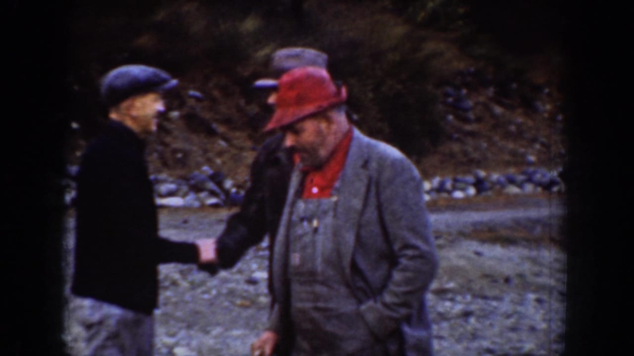 Two men, one in a dark flat cap and one in a red wide-brim hat, converse at an outdoor mountain-area location, circa 1939.
