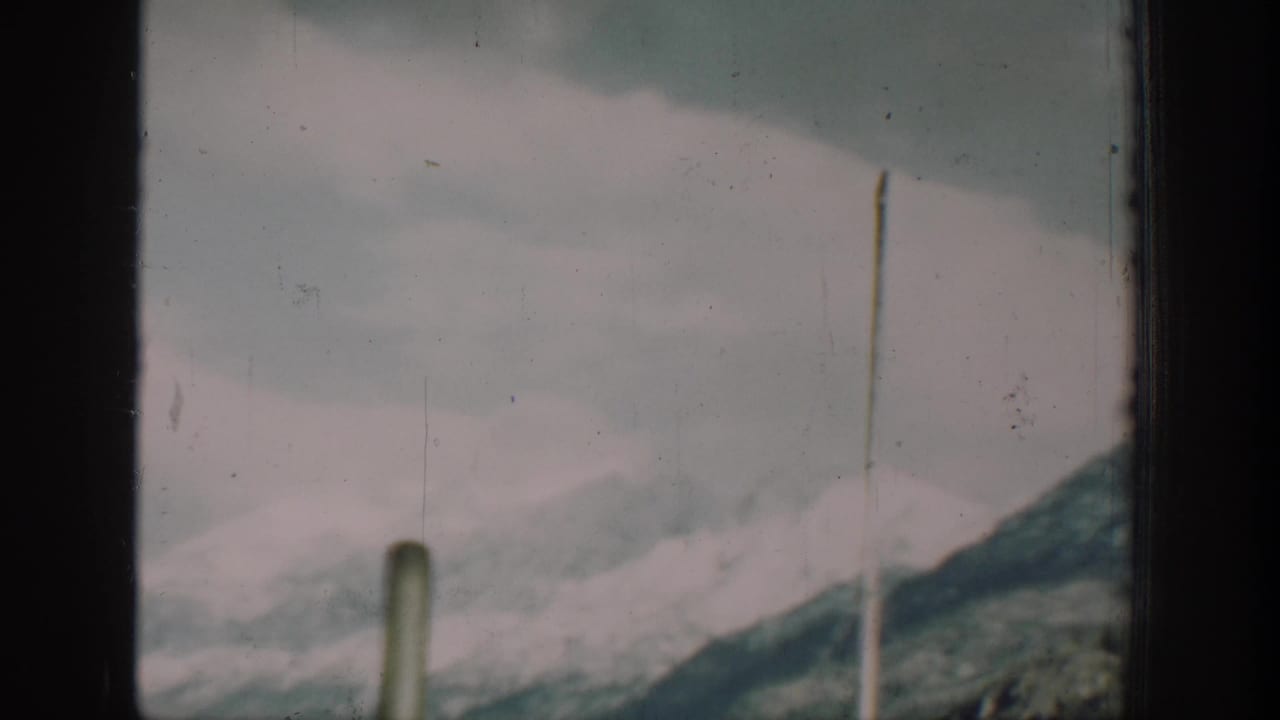 Two vertical boat deck poles silhouetted against a pale overcast sky with snow-dusted mountain slopes in the background.