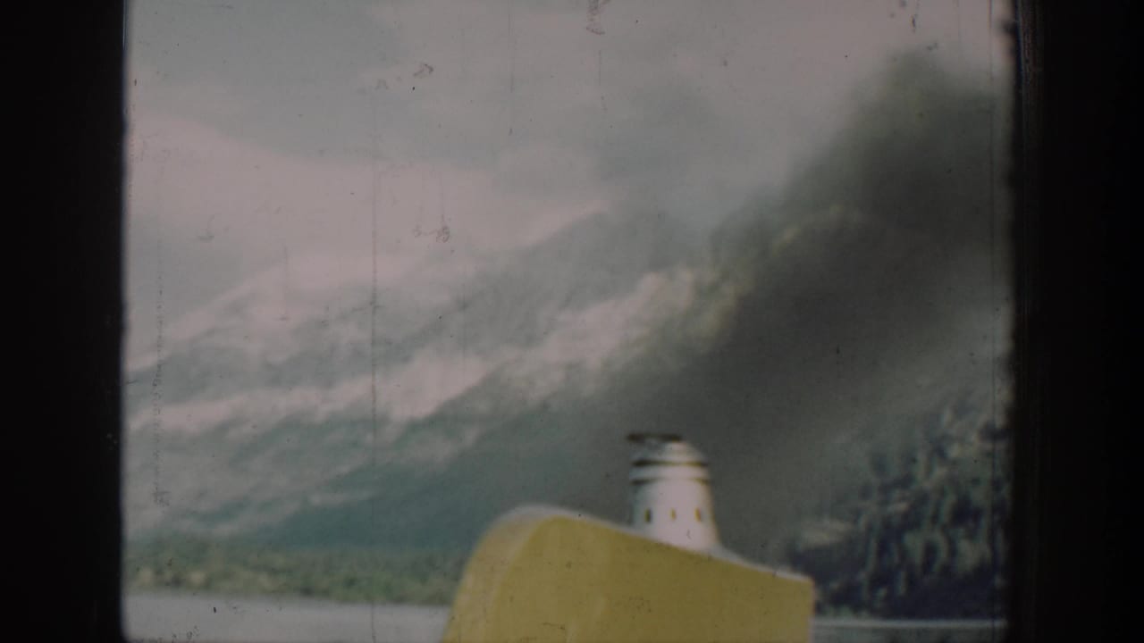 8mm home-movie frame from a 1939 Lake Chelan, Washington boat journey, showing yellow hull and white smokestack with mountain backdrop viewed through a cabin window.