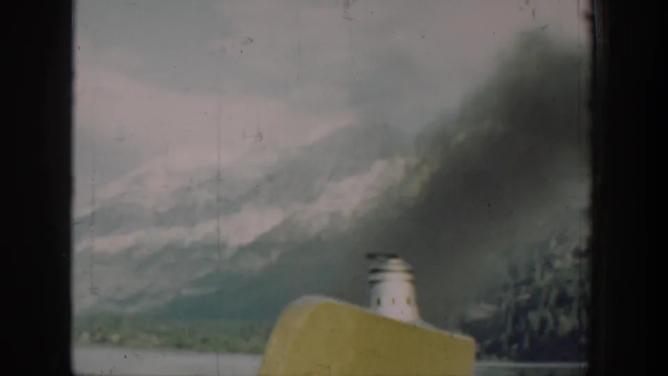 8mm home-movie frame from a 1939 Lake Chelan, Washington boat journey, showing yellow hull and white smokestack with mountain backdrop viewed through a cabin window.