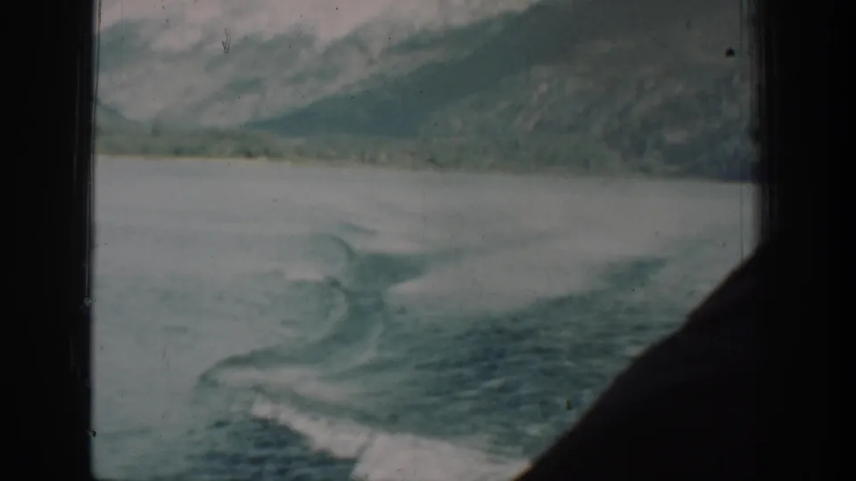 8mm footage from a 1939 Lake Chelan steamer journey showing the vessel's wake and distant forested mountains through a cabin porthole.
