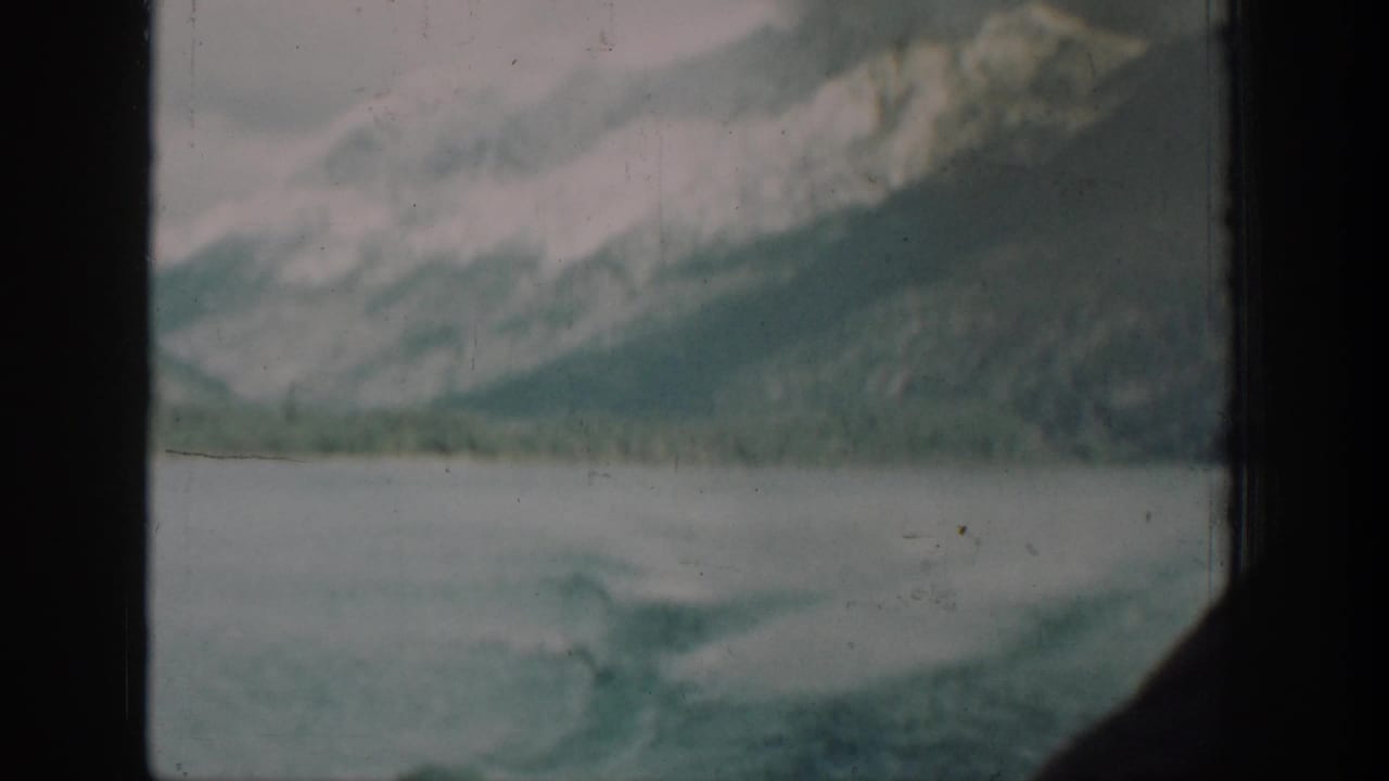 8mm home-movie shot from aboard a 1939 Lake Chelan vessel, capturing the wake and mist-covered mountains through a cabin window.