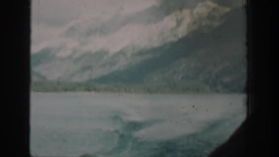 8mm home-movie shot from aboard a 1939 Lake Chelan vessel, capturing the wake and mist-covered mountains through a cabin window.