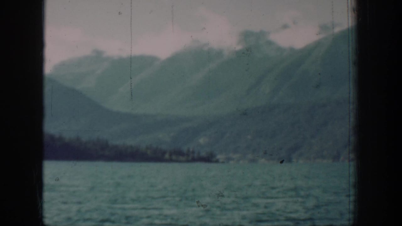 8mm home-movie frame from a 1939 Lake Chelan journey, showing calm lake water and conifer-covered mountain slopes through a cabin porthole.