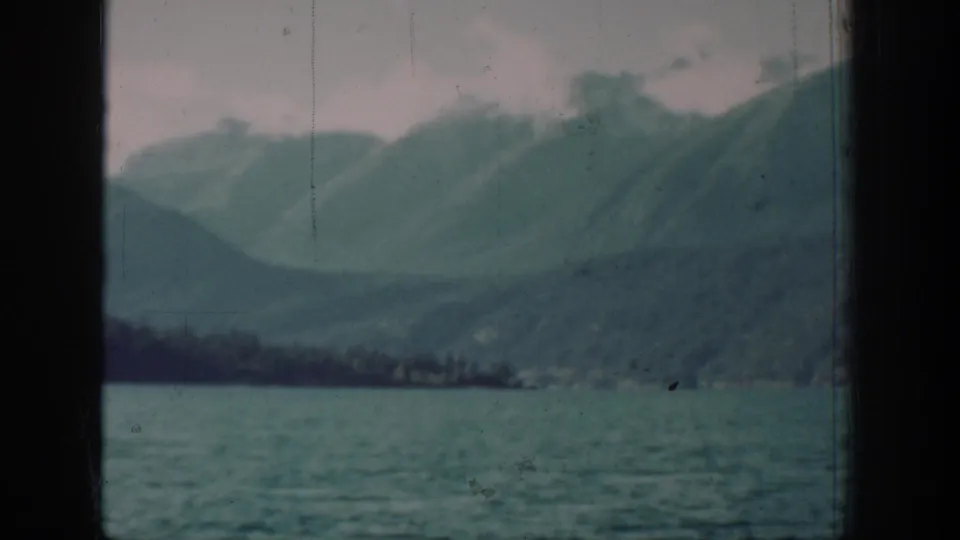 8mm home-movie frame from a 1939 Lake Chelan journey, showing calm lake water and conifer-covered mountain slopes through a cabin porthole.