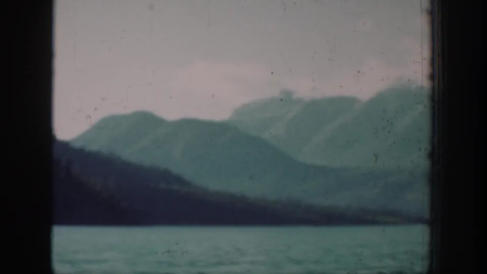 Archival 8mm shot of the Lake Chelan area, Washington, showing a mountain ridgeline and calm lake surface with slight reframing and dark vignetting on the left edge.