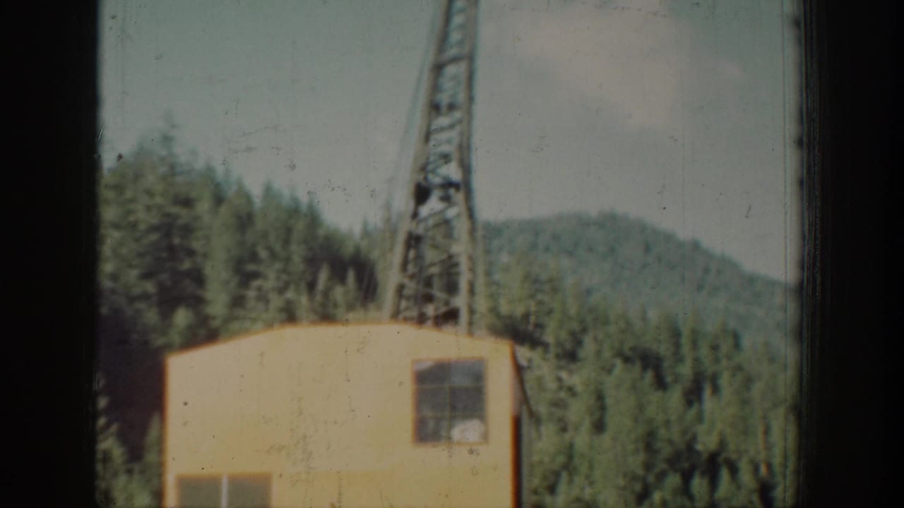 A lattice steel crane or derrick rises beside a small yellow outbuilding, set against a steep forested mountain ridge, ca. 1939, Washington state