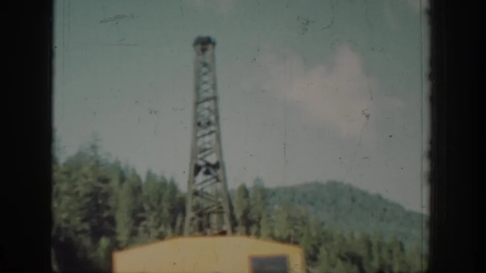 Yellow crane with steel lattice tower rising above conifer forest, Chelan, Washington, circa 1939, 8mm home movie