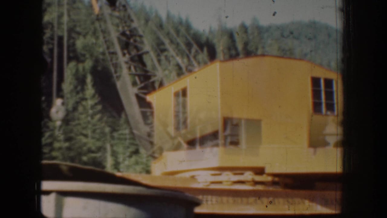 Yellow crane operator cabin and lattice boom amid Pacific Northwest conifers, Chelan area, circa 1939, 8mm home movie