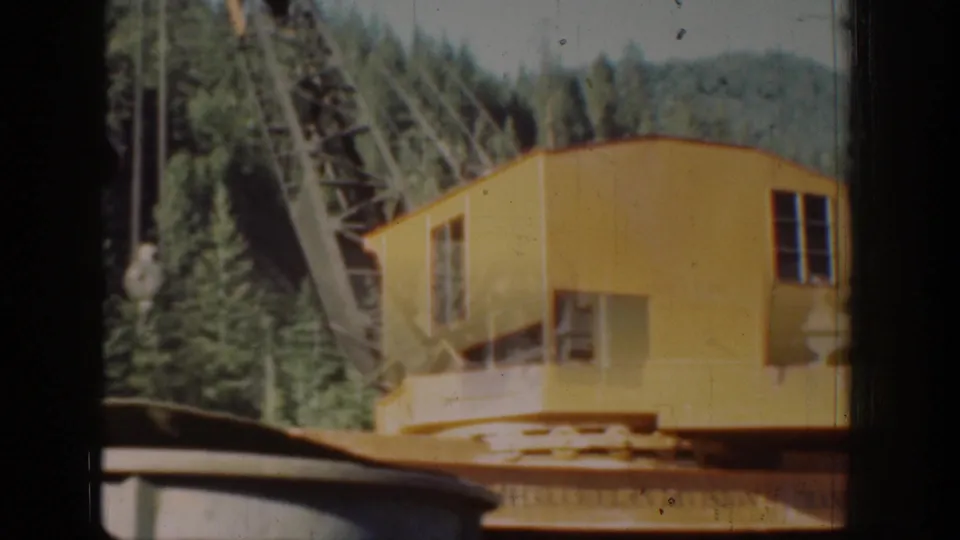 Yellow crane operator cabin and lattice boom amid Pacific Northwest conifers, Chelan area, circa 1939, 8mm home movie