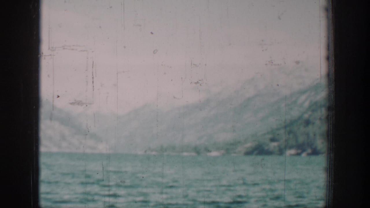 Late-1930s 8mm home movie frame showing a pale mountain lake and forested slopes, possibly Lake Chelan, Washington, with visible film scratches.
