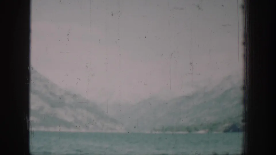 Heavily overexposed or degraded 8mm film frame showing a faint mountain and lake silhouette; likely a transition or damaged section of the reel.