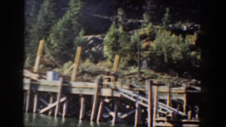 8mm color home-movie frame circa 1939 showing a timber pier structure at Lake Chelan, Washington, backed by an evergreen-covered rocky hillside.