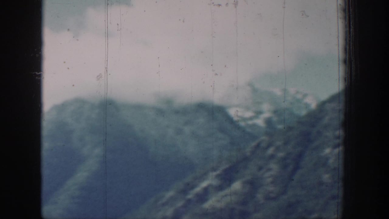 Steep mountain ridgeline against a hazy pale sky, filmed in early color 8mm with visible color fading.