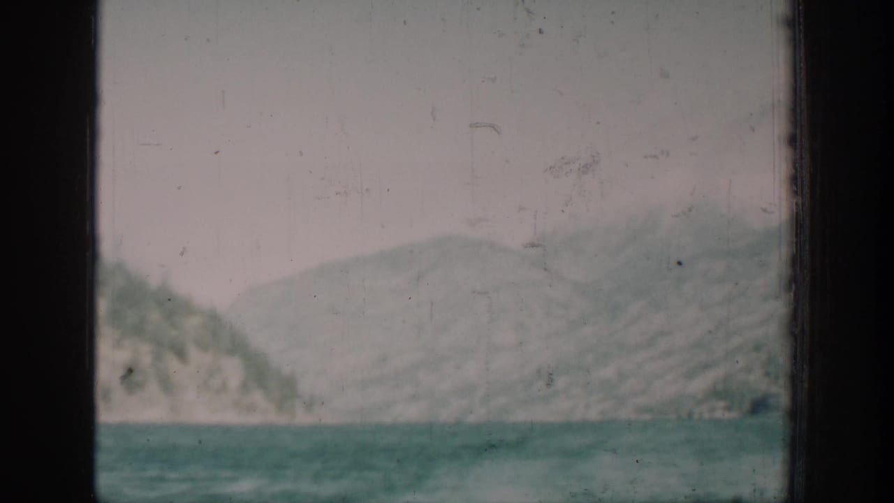 Mountain range and lake viewed past a window edge, 8mm color film with teal cast and visible grain.