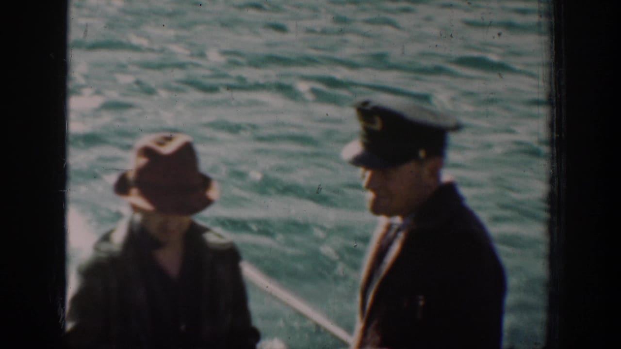 Two men in period coats and hats conversing on an open boat deck with choppy blue-green water behind them, color 8mm, circa 1939.