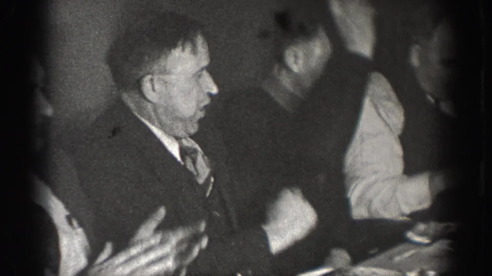 Men at an informal dinner gathering in Chelan, Washington, circa 1939; foreground man gesturing animatedly in conversation; characteristic 8mm film vignetting.