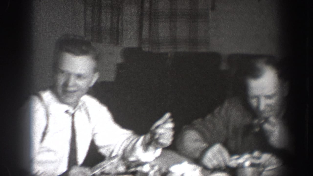 Man laughing and gesturing at a dinner table, Chelan, Washington, circa 1939; overexposed center typical of 8mm indoor available-light shooting; curtains in background.