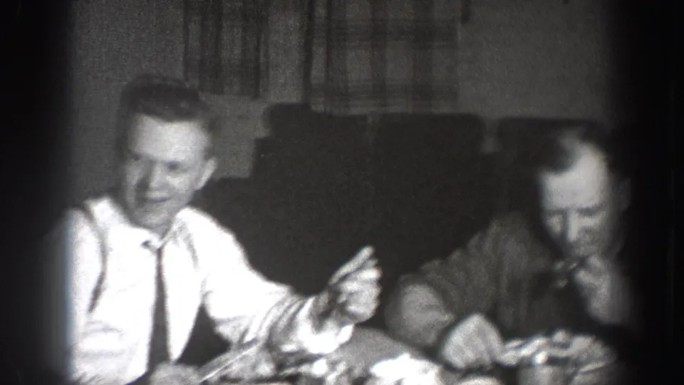 Man laughing and gesturing at a dinner table, Chelan, Washington, circa 1939; overexposed center typical of 8mm indoor available-light shooting; curtains in background.