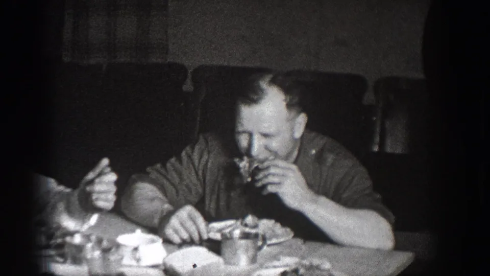 Man eating at an informal dinner gathering, Chelan, Washington, circa 1939; plates and food on the table; deep 8mm vignetting typical of this era and format.
