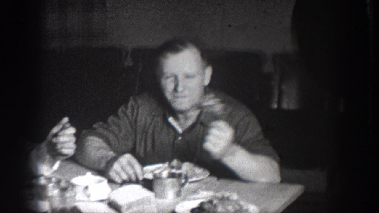 Man at dinner table, Chelan, Washington, circa 1939; holding utensil with plates of food visible in foreground; characteristic 8mm film vignetting and grain throughout.