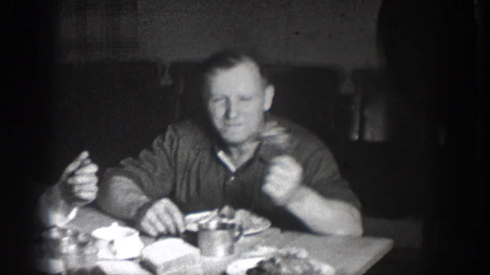 Man at dinner table, Chelan, Washington, circa 1939; holding utensil with plates of food visible in foreground; characteristic 8mm film vignetting and grain throughout.