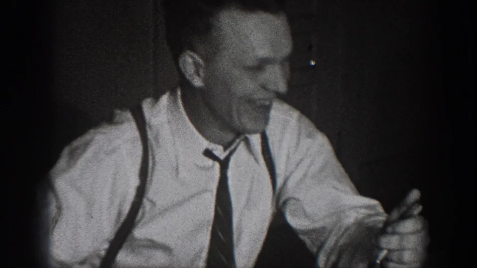 Close-up of man in white dress shirt, suspenders, and dark necktie smiling at dinner; late 1930s dress, Chelan, Washington home movie.