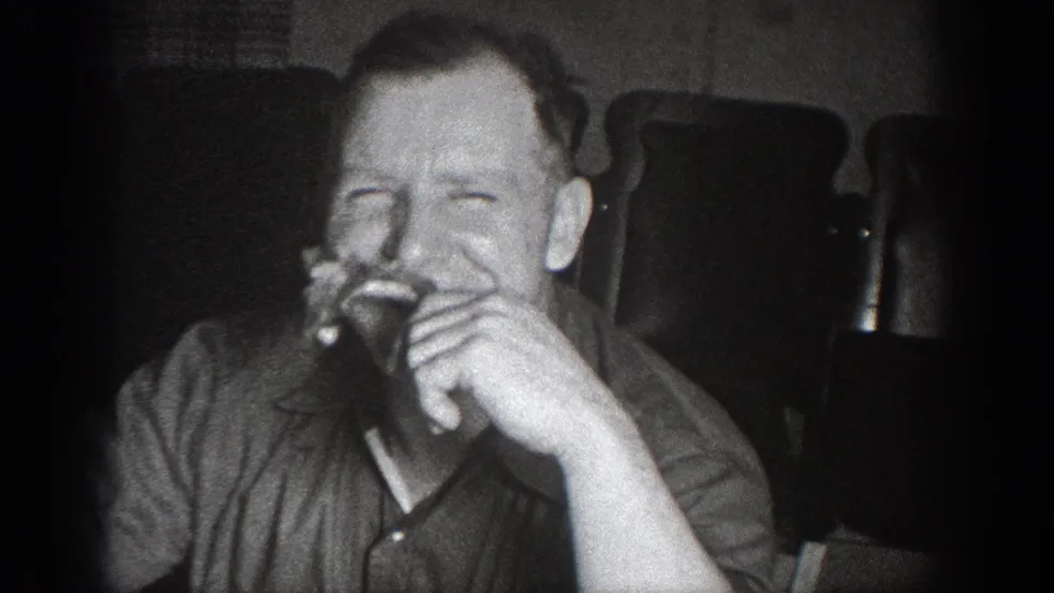 Man in dark collared shirt laughing while eating in a candid home movie moment; circa 1939, attributed to Chelan, Washington.