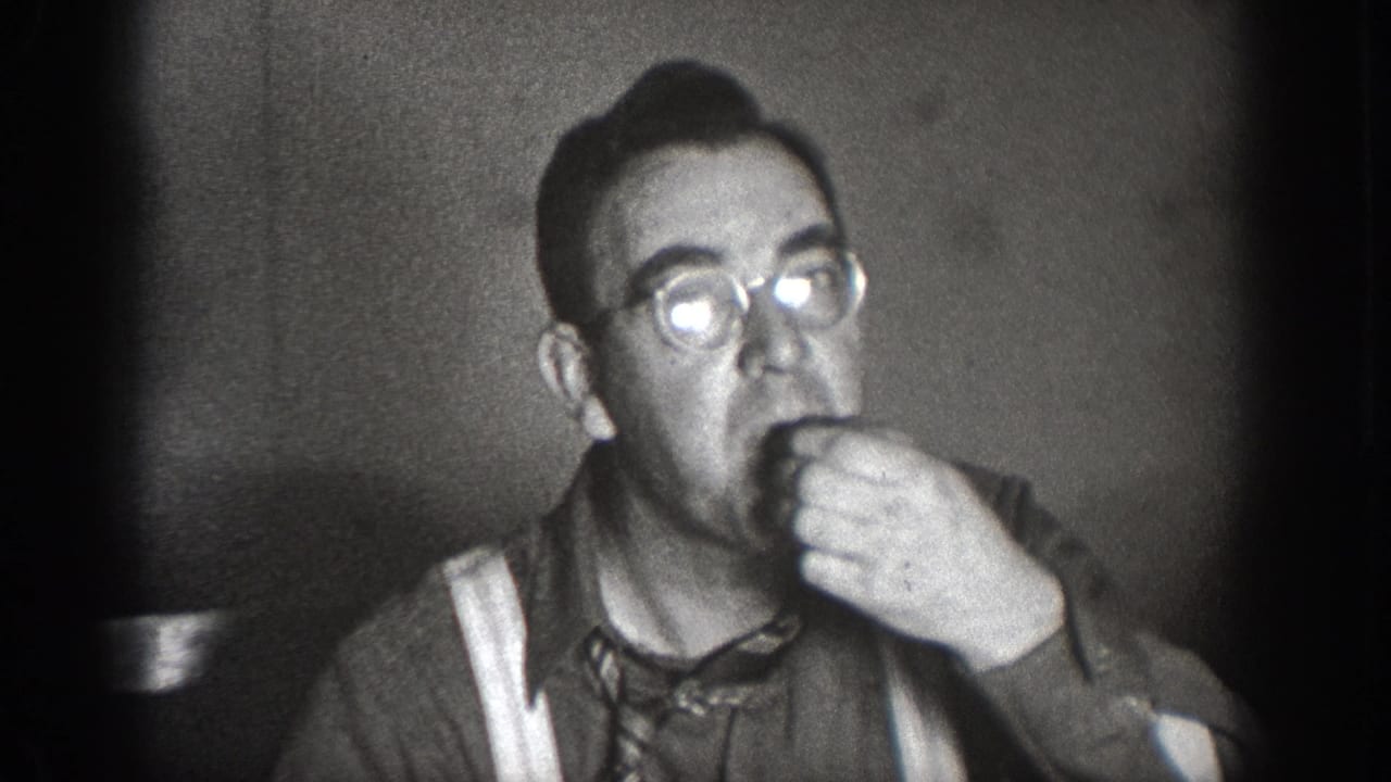 Man wearing round glasses, suspenders, and necktie eating or drinking at an indoor gathering, Chelan, Washington, circa 1939; black-and-white 8mm home movie.