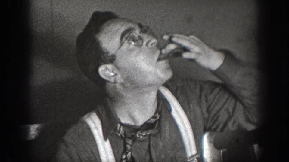 Man in suspenders and necktie tilting his head back to drink at an indoor gathering, Chelan, Washington, circa 1939; 8mm home movie.